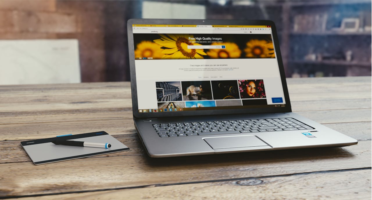 experience-img Laptop with open webpage on wooden desk, accompanied by tablet and pen, representing digital work setup.