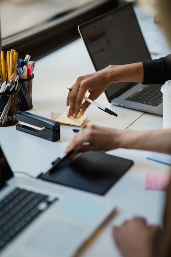 Close-up of hands using office supplies on a desk with laptops and stationery.