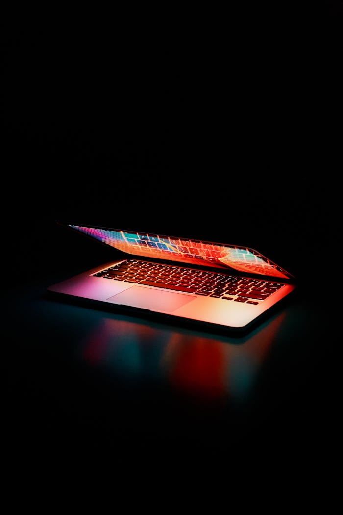 about-me-02 Laptop partially opened, emitting vibrant multicolored lights in dark setting.