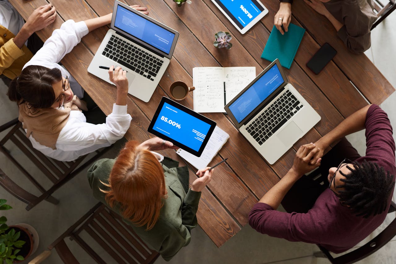 services-03 Diverse team discussing business strategies with laptops and tablets at a wooden table.